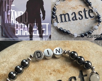 May include: A silver bracelet with black beads and white stones. The bracelet has the letters "DIN" spelled out on it. The bracelet is on a stone surface with the word "amaster" written on it.