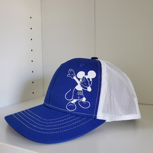 May include: A blue and white trucker hat with a white Mickey Mouse graphic doing the dab. The graphic includes the text "00".