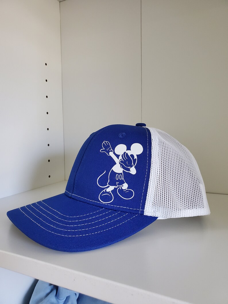 May include: A blue and white trucker hat with a white Mickey Mouse graphic doing the dab. The graphic includes the text "00".
