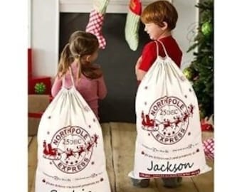Peut inclure: Deux sacs de Noël en toile blanche avec des motifs rouges North Pole Express. Les sacs portent des noms personnalisés, Sophia et Jackson, imprimés en bas.