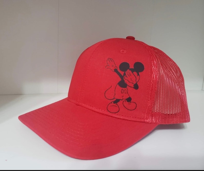 May include: Red and black baseball cap with a mesh back. The front of the cap features a black and white image of Mickey Mouse doing the dab.