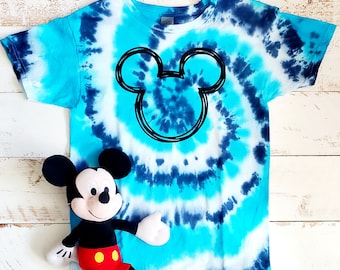 Peut inclure: Un t-shirt bleu et blanc tie-dye avec un contour noir de la tête de Mickey Mouse au centre.