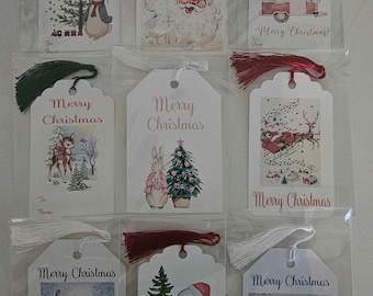 Peut inclure: Neuf étiquettes cadeaux blanches avec des glands rouges et verts. Chaque étiquette présente une illustration de Noël vintage différente, notamment le Père Noël, un bonhomme de neige, un cerf et un sapin de Noël. Les étiquettes portent le texte "Merry Christmas" imprimé dessus.