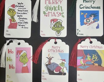 Peut inclure: Ensemble de six étiquettes cadeaux blanches avec des illustrations et du texte sur le thème du Grinch. Les étiquettes présentent des citations, les mots "Merry Grinchmas" et "Merry Christmas", et des images du Grinch. Chaque étiquette a un pompon.