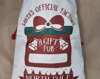 Peut inclure: Un sac de Noël en toile blanche avec un cordon de serrage rouge. Le sac a un motif rouge et vert d'une boîte cadeau avec un nœud, des cloches et le texte "Santa's Official Factory A Gift For North Pole Express Delivery".