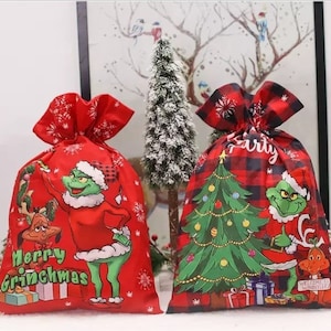 Könnte beinhalten: Zwei rote Weihnachtsgeschenktüten mit einem Grinch-Motiv. Eine Tasche hat ein rot-schwarzes Karomuster und die andere einen roten Hintergrund mit weißen Schneeflocken. Beide Taschen zeigen den Grinch und Max den Hund.
