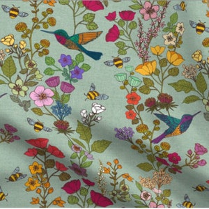 Op de afbeelding: Een tealblauwe stof met een herhalend patroon van kolibries, bijen en bloemen in verschillende kleuren, waaronder roze, geel, rood en groen.