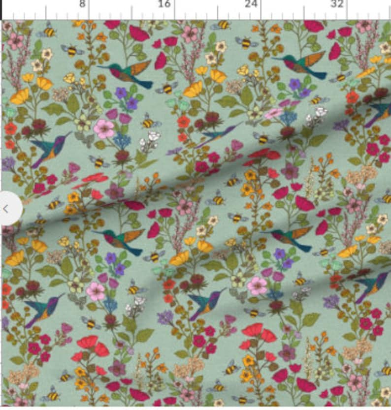 Op de afbeelding: Een tealblauwe stof met een herhalend patroon van kolibries, bijen en kleurrijke bloemen. De kolibries vliegen en de bijen zoemen rond de bloemen.