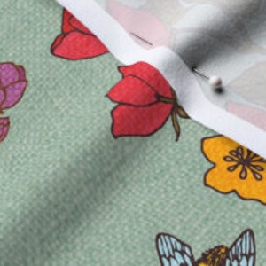 Op de afbeelding: Groene stof met een bloemen- en bijenprint. De bloemen zijn rood, roze, geel en oranje. De bij is blauw en geel.