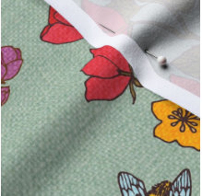 Op de afbeelding: Groene stof met een bloemen- en bijenprint. De bloemen zijn rood, roze, geel en oranje. De bij is blauw en geel.