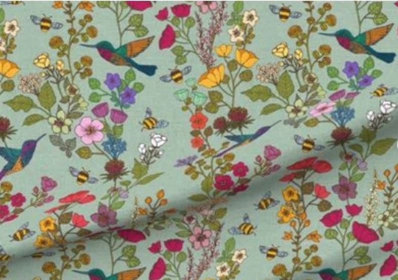 Op de afbeelding: Een tealblauwe stof met een herhalend patroon van kolibries, bijen en bloemen in tinten roze, rood, geel, groen en paars.