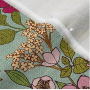 Op de afbeelding: Close-up van een bloemenstof met een witte rand. De stof heeft een lichtblauwe achtergrond met roze en gele bloemen en groene bladeren.