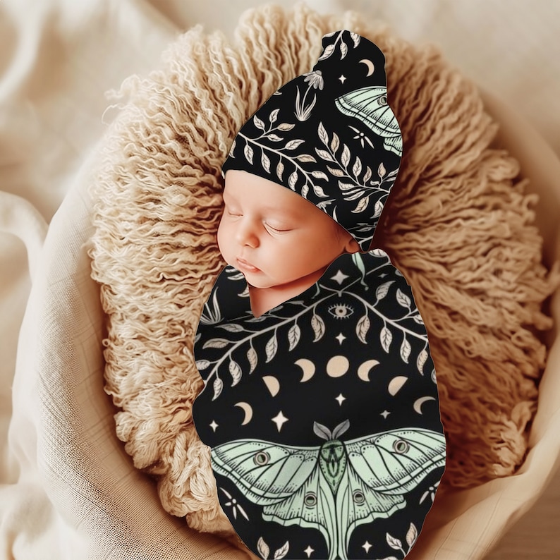 May include: A black and white swaddle with a green moth design and a matching black and white hat with a floral pattern. The swaddle and hat are made of soft, comfortable fabric and are perfect for a newborn baby.