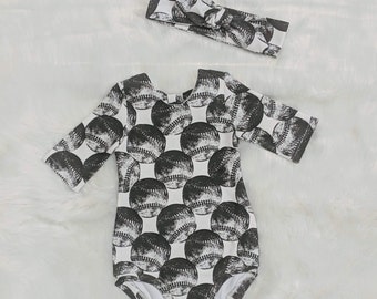 May include: A white bodysuit with a black and white baseball print. The bodysuit has a long sleeve and a snap closure. A black and white headband is included.