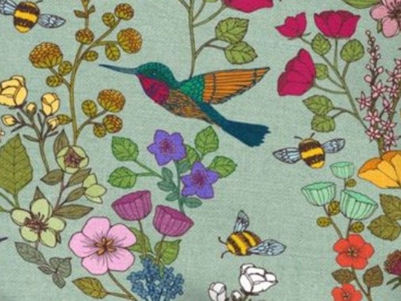 Op de afbeelding: Een tealblauwe achtergrond met een kolibrie die over een bloemenpatroon vliegt. De bloemen zijn in tinten roze, paars, rood, geel en wit. Er vliegen ook bijen rond de bloemen.