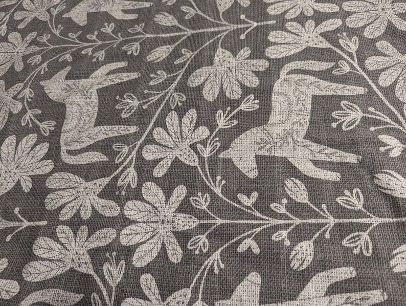 May include: A grey fabric with a white repeating pattern of stylised animals and floral designs. The animals resemble deer or horses with long legs and necks.