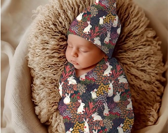 May include: A baby swaddle blanket and matching beanie hat featuring a dark navy blue background with a repeating pattern of white rabbits, colorful flowers, and green foliage. The fabric has a dense, vibrant floral print with small white bunnies.
