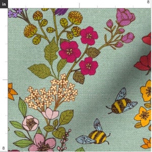 Op de afbeelding: Een tealblauwe stof met een bloemenpatroon met roze, gele en oranje bloemen, groene bladeren en twee hommels.