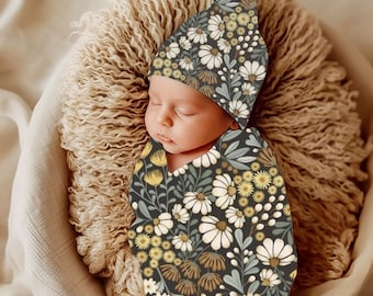 May include: A newborn baby swaddled in a dark gray and white floral swaddle with a matching floral beanie. The baby is sleeping peacefully in a fluffy brown nest.
