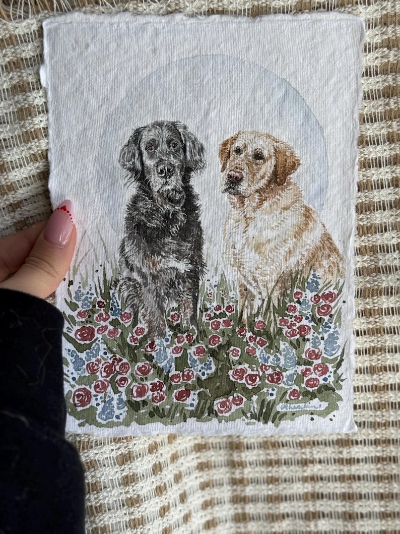 以下が含まれることがあります： 2匹の犬の水彩画。1匹は黒、もう1匹は金色で、花畑に座っています。このアートワークは、淡い青色の背景と赤、青、緑の花の要素を備えた、柔らかく絵画的なスタイルです。