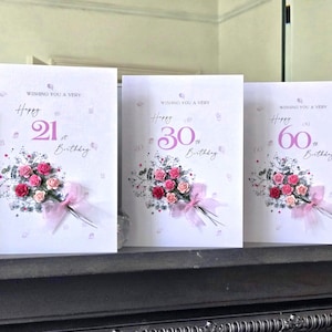 Op de afbeelding: Drie verjaardagskaarten met bloemboeketten en de tekst "Wishing You a Very Happy 21st, 30th, and 60th Birthday." Elke kaart heeft roze en rode rozen met een roze lint.