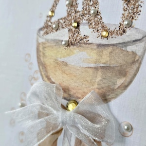 May include: A handmade greeting card featuring a champagne glass illustration with the number "40" in gold glitter and embellished with pearls and gold gems. A white sheer bow is attached to the glass, adding a touch of elegance. The card is perfect for a 40th birthday celebration.