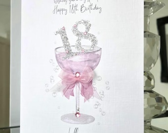 May include: A white greeting card with a watercolor illustration of a pink cocktail glass, a pink bow, and the number "18" in silver glitter. The card reads "Wishing you a very special Happy 18th Birthday" and is signed "Lilly".