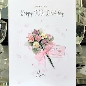 May include: A white card with the text "With Love Happy 90th Birthday Mum" and a pink bouquet of flowers with a tag that says "90 Today".
