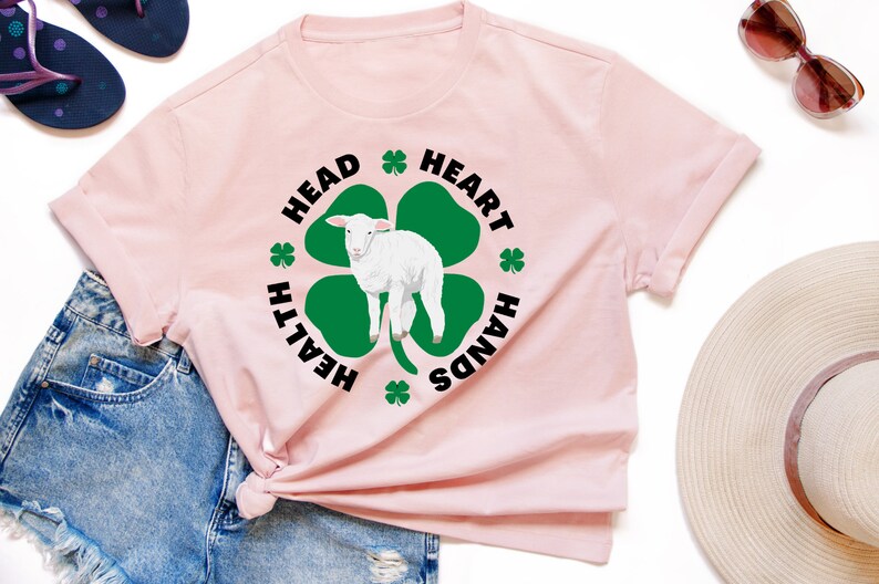 May include: A pink t-shirt with a black and green shamrock design. The shamrock has a white lamb inside and the words "Health", "Head", "Heart", and "Hands" around it.