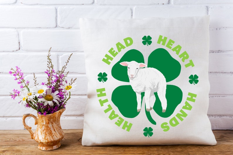 May include: White throw pillow with a green shamrock design and the text "Head, Heart, Hands, Health" around the shamrock. A white lamb is standing in the center of the shamrock.