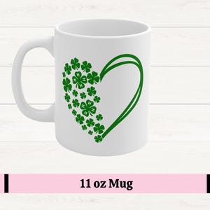 May include: White ceramic mug featuring a green heart design composed of shamrocks. The mug has a curved handle and the text "11 oz Mug" is displayed at the bottom. The shamrocks are a symbol of good luck and are often associated with St. Patrick's Day.