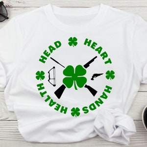 May include: White t-shirt with a black and green design. The design features a four-leaf clover, two crossed rifles, a bow and arrow, and the text "HEAD HEALTH HANDS HEART" in a circle around the clover.
