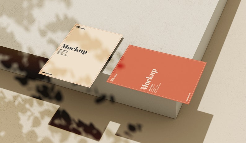May include: Two blank cards with the word "Mockup" printed on them. The cards are on a light brown surface with a shadow from a plant.