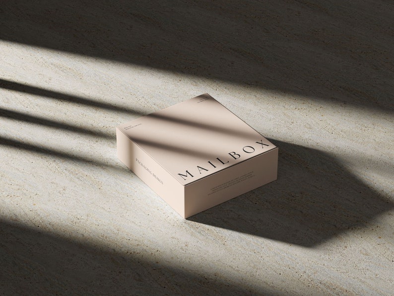 May include: A square, light beige cardboard box featuring the word MAILBOX printed in black serif font on the top surface. The box has additional small black text on the side and top, including the phrase PACKAGING DESIGN.