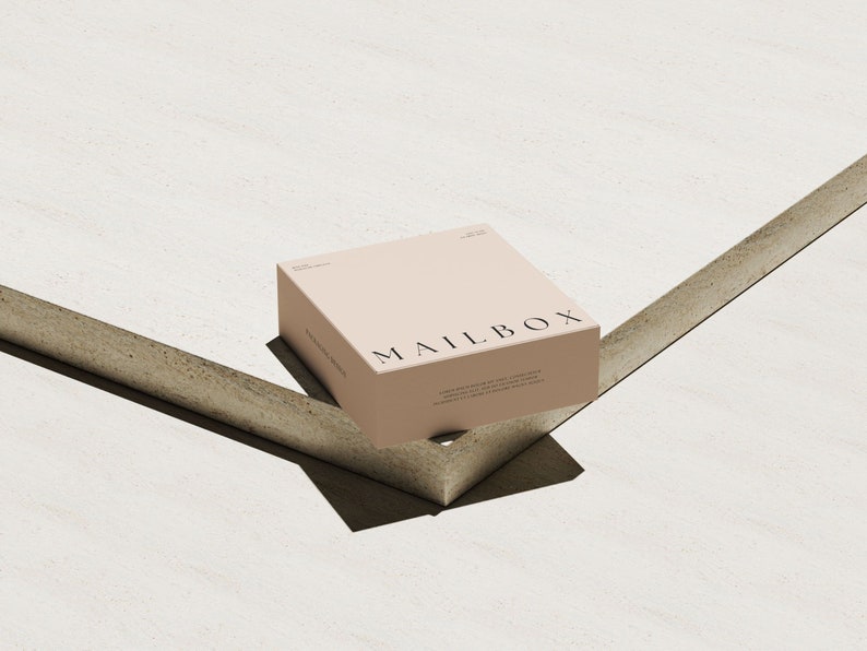 May include: A square, light beige cardboard box with the word MAILBOX printed in black capital letters on the top surface. The box features additional small black text printed on the top and side panels, presenting a clean and simple design.