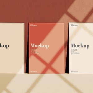May include: Three A4 poster mockups on a brown textured wall. The posters are white, cream, and a light orange color. Each poster has the word "Mockup" printed in black text. The posters are in a row, with the white poster on the left, the cream poster in the middle, and the orange poster on the right.