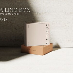 May include: A light beige square mailing box with the word MAILBOX printed vertically in black on the side, resting on a flat tan cardboard box base. The text MAILING BOX PACKAGING MOCKUPS 8 PSD is visible in the upper left corner of the image.