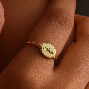 May include: A gold oval ring with the name "Rosa" engraved on it.