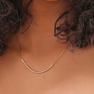 May include: A close-up of a person with curly brown hair smiling. They are wearing a gold necklace with small beads.