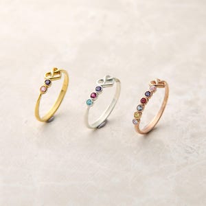 May include: Three rings with a crown design and colorful gemstones. The rings are gold, silver, and rose gold. Each ring has a different arrangement of gemstones, including purple, pink, red, and blue.