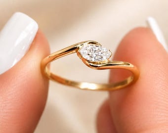 Pode incluir: Um anel de ouro com uma única pedra preciosa transparente de corte marquise montada numa banda de estilo bypass. A banda de ouro amarelo polido curva-se em torno da pedra alongada, criando um design elegante e contínuo que destaca a gema branca.