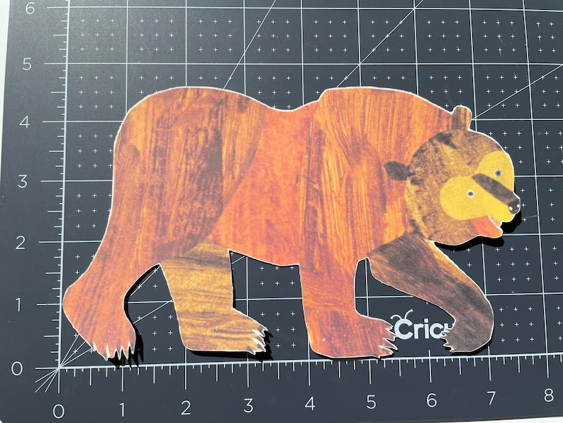 Pu&ograve; includere: Un ritaglio di orso marrone con naso e bocca gialli, che cammina verso destra. L'orso &egrave; fatto di carta con un motivo a venature di legno.