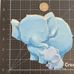 May include: Two blue felt elephants, one larger than the other, are hugging. The larger elephant has its eyes closed and the smaller elephant is looking up at the larger elephant.