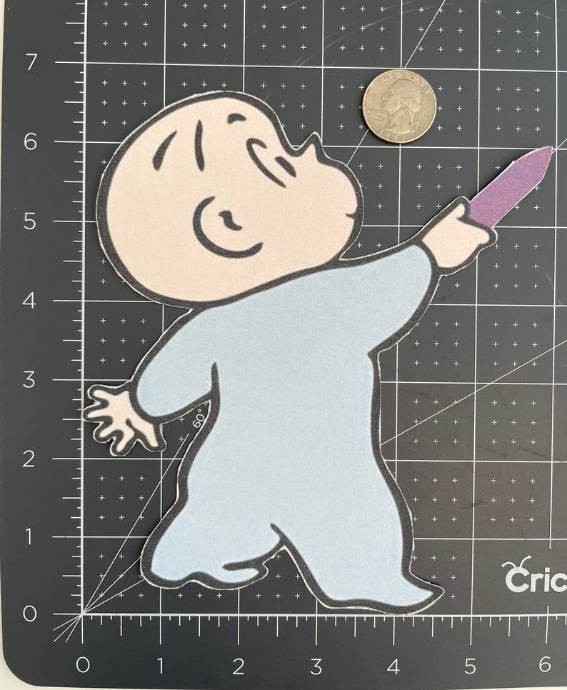 May include: A light blue felt applique of a cartoon baby holding a purple crayon. The baby has a large head with a round face and large eyes. The baby is wearing a blue onesie.