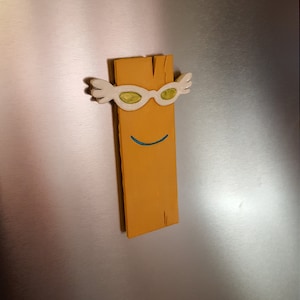 May include: A yellow wooden plank with a smiling face and white sunglasses with green lenses. The plank is a character from the cartoon show "The Backyardigans".