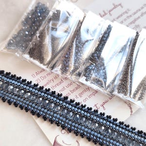 May include: A beaded bracelet featuring rows of dark gray, light blue, and clear faceted beads with a metallic finish. The bracelet is accompanied by five small clear plastic bags containing loose matching beads and a printed instruction card.