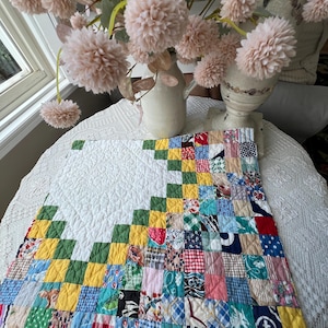 May include: A square patchwork quilt featuring a large white quilted section on the left and a vibrant grid of multi-colored fabric squares on the right. The colorful section includes various patterns in red, yellow, green, blue, and pink tones.