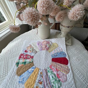 May include: A square white quilted fabric mat featuring a central circular white quilted section surrounded by a ring of sixteen multi-colored fabric petals in various patterns including stripes, floral prints, plaids, and solid colors.