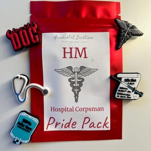 Op de afbeelding: Een rode zak met de tekst "Accidental Creations Est. 2020 HM Hospital Corpsman Pride Pack" en vijf zwart-witte medische schoenbedels. De bedels omvatten een stethoscoop, een caduceus, een infuuszak, een spuit en een rol met de tekst "Hit list".