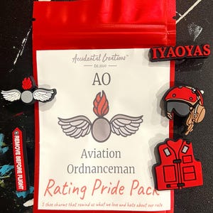 May include: A set of five red, white, and gray shoe charms with the text "Aviation Ordnanceman Rating Pride Pack" and "REMOVE BEFORE FLIGHT". The charms are shaped like a winged bomb, a pilot's helmet, a life vest, and the text "IYAOYAS".